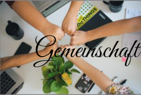 Fünf Menschen stoßen ihre Fäuste über einem Schreibtisch zusammen – ein Symbol für Zusammenhalt und Teamgeist; im Vordergrund eine Pflanze und der Schriftzug „Gemeinschaft“.